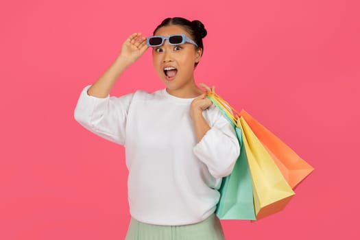 Asian Woman With Shopping Bags Taking Off Sunglasses And Looking At Camera