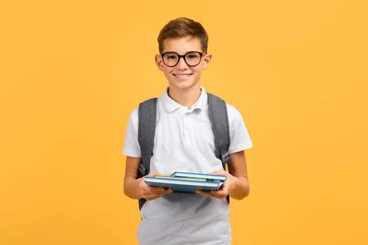 Happy teen boy wearing glasses and backpack holding workbooks