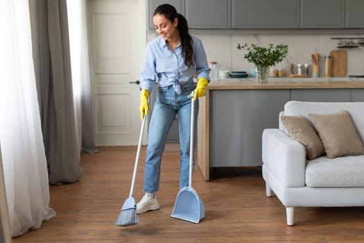 Woman with broom and dustpan cleaning the wooden floor