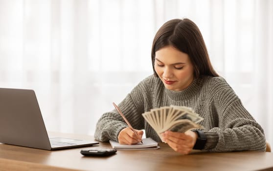 Happy young woman budgeting with cash and calculator at desk