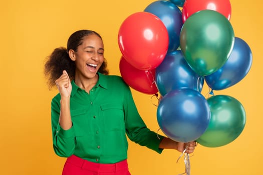 African adolescent girl posing with bright festive helium balloons, studio