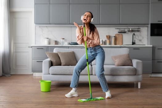Woman singing into mop like a microphone, enjoying cleaning