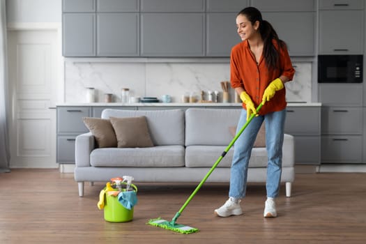 Smiling woman mopping floor with a bucket of supplies nearby