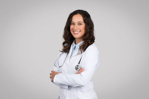 Portrait of confident female doctor in medical white uniform coat and stethoscope, posing with folded arms and smiling