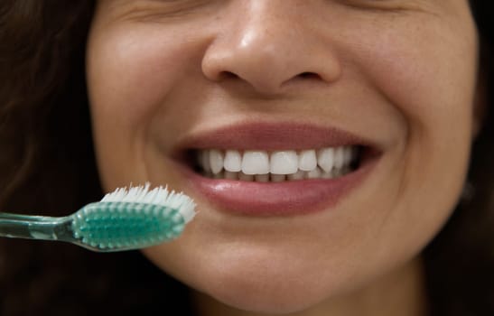Extreme close-up of the beautiful smile of a woman with clean white teeth, holding a toothbrush near her mouth