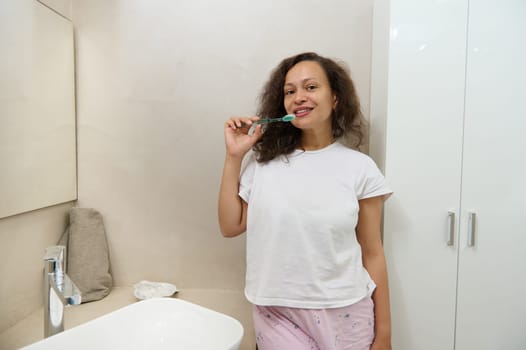Beautiful woman holding a toothbrush near her mouth, smiling, looking at camera. Oral care and dental hygiene