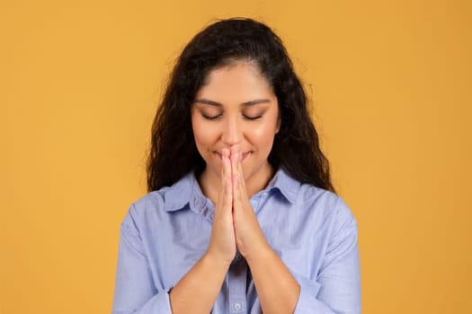 Contemplative young woman with eyes closed and hands pressed together in a prayerful