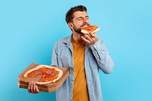 Young Guy Eating Slice Of Pizza Posing With Box, Studio