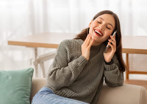 Joyful lady talking on phone and laughing, home interior