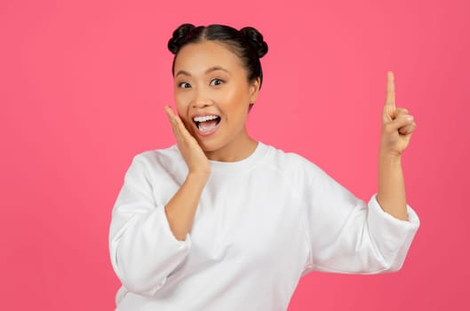 Excited asian woman with hair buns pointing upwards with finger