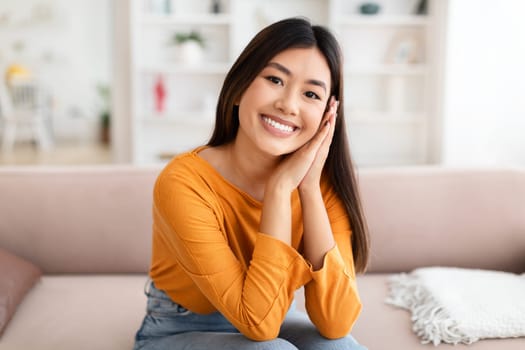 Cute pretty chinese lady sitting on couch at home
