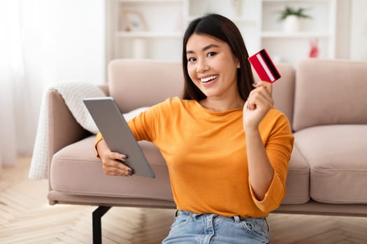 Positive young asian woman using credit card and digital tablet