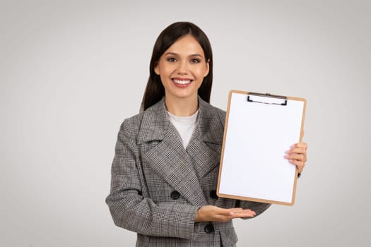 Smiling woman presenting blank clipboard for design