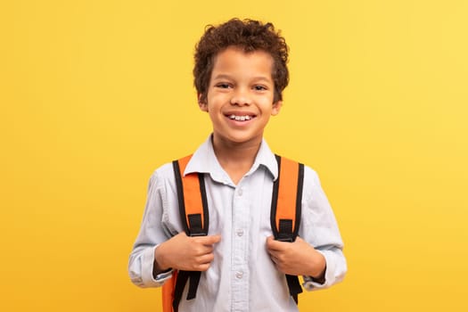 Cheerful latin schoolboy with backpack on yellow background