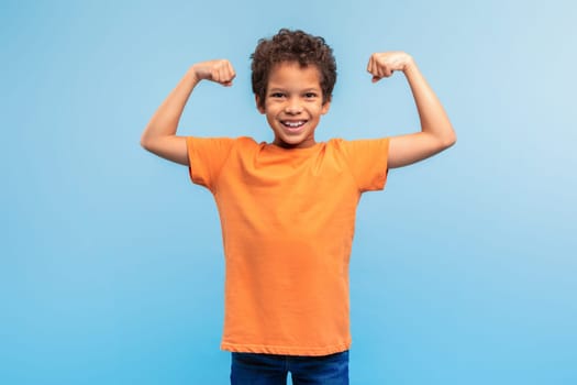 Strong, confident boy flexing muscles on blue background