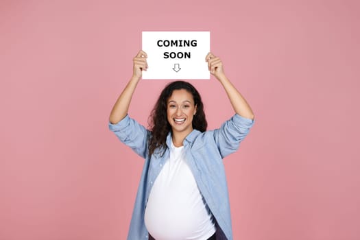 pleased and pregnant woman holding board with coming soon lettering