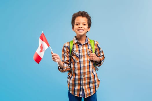 Happy boy with Canadian flag and backpack, blue backdrop