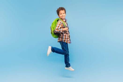 Boy in mid-stride with backpack, cheerful on blue background