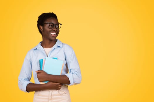 Glad black young lady student in glasses, with books, look at copy space