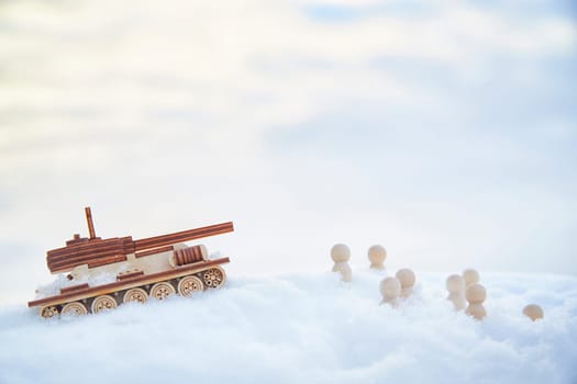 A wooden toy tank and little men in the snow. Russia and Ukraine are at war in winter. Encirclement, retreat, attack, victory