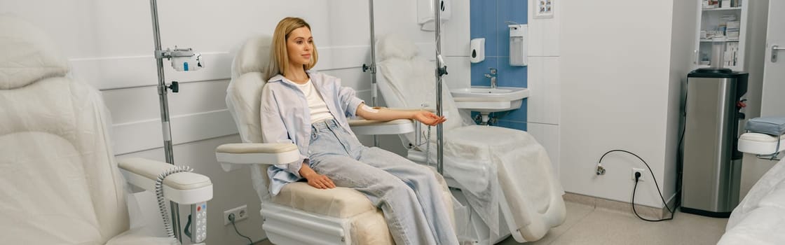 Pretty woman patient sitting in armchair while receiving IV infusion during treatment in hospital
