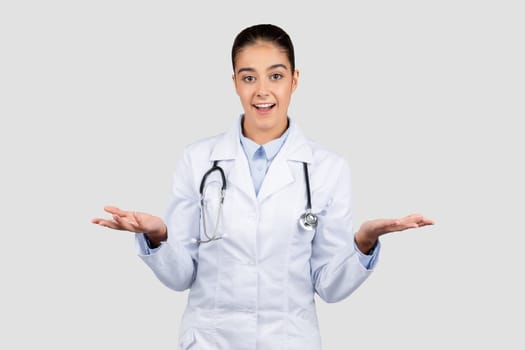 A surprised female doctor in a white coat with a stethoscope gestures with her hands open