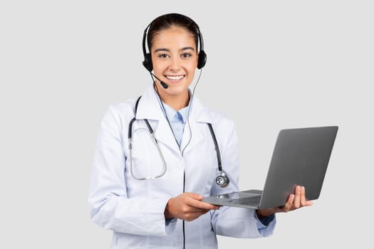 A friendly european doctor with a headset and microphone, holding an open laptop