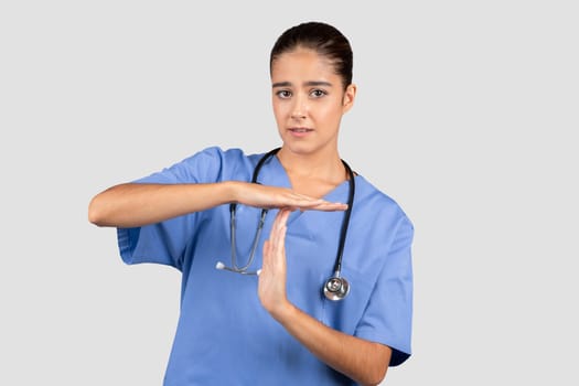 Concerned european nurse in blue scrubs making a timeout sign with her hands, indicating a need for a pause