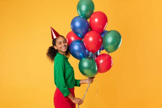 Happy black teen girl in birthday hat holding balloons, studio