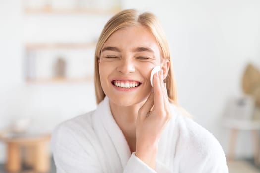 Funny Blonde Woman Doing Facial Skincare With Cotton Pad Indoors