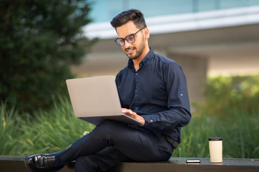 Young Arabian businessman engaged in distance work on laptop outside
