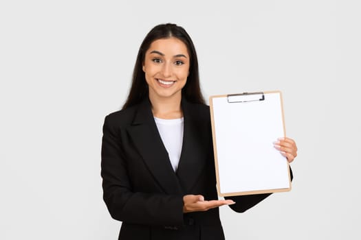 Happy young business lady holding blank clipboard and showing place for design or signing contract