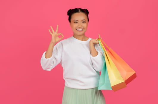 Big Sales. Happy Asian Female Holding Shopping Bags And Showing Ok Gesture