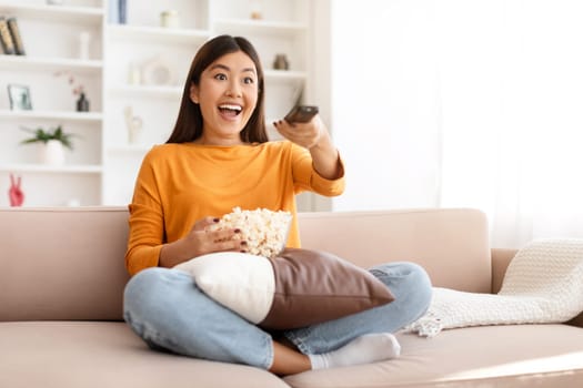 Excited young asian woman watching her favorite TV show