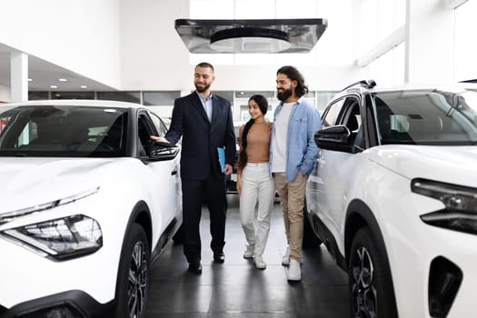 Young indian loving couple choosing car at luxury auto dealership
