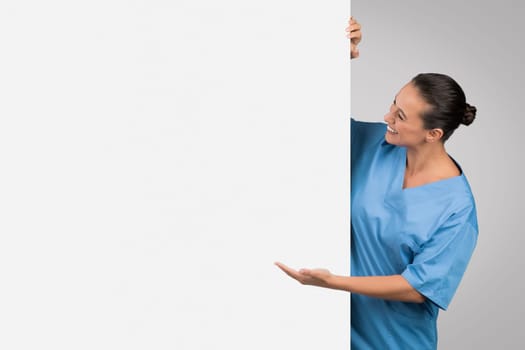 Medical ad. Young european woman physician demonstrating empty space on white placard, showing place for your design