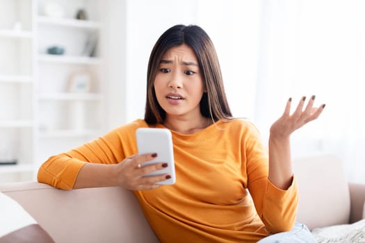 Furious young chinese woman looking at phone, gesturing