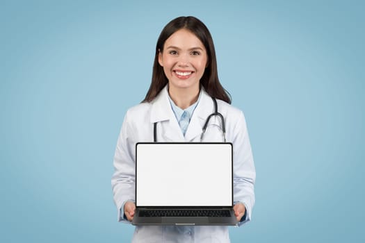 Happy female doctor showcasing laptop with blank screen, symbolizing the ease of access to e-health services and medical advertisement
