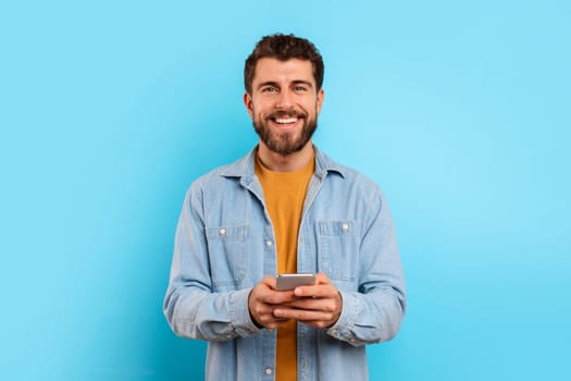 Cheerful guy with smartphone looking at camera and smiling, studio
