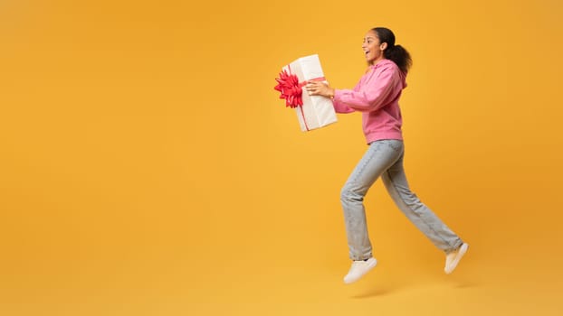 Cheerful African American teen lady offering wrapped present box, studio