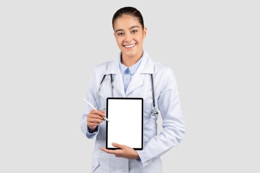 A cheerful female doctor in a lab coat and stethoscope holds a tablet with a stylus