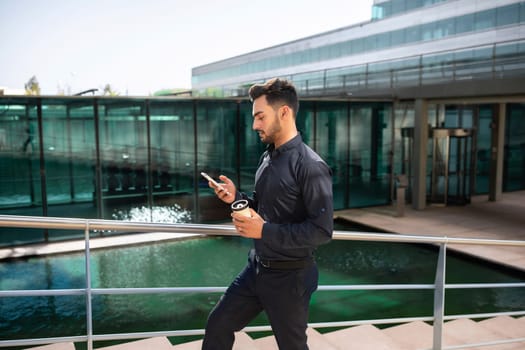 Successful arab businessman with takeaway coffee, using phone walking outdoor