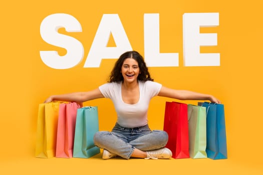 indian woman sitting with purchases over yellow background word SALE