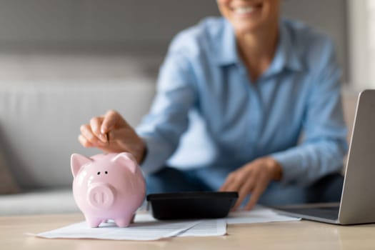 Unrecognizable senior woman putting money in piggybank at home, cropped