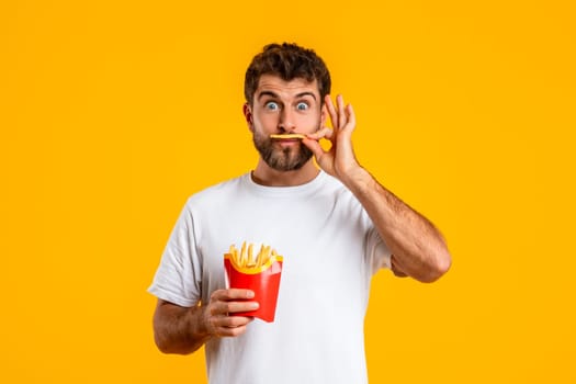 Funny Hungry Man Tasting French Fries Posing Over Yellow Background