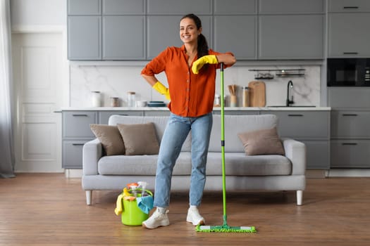 Confident woman with mop and cleaning gear in stylish kitchen