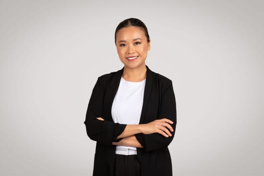Confident young Asian businesswoman with arms crossed wearing a black blazer