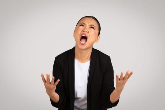 Desperate Asian businesswoman with an anguished expression, hands up in the air