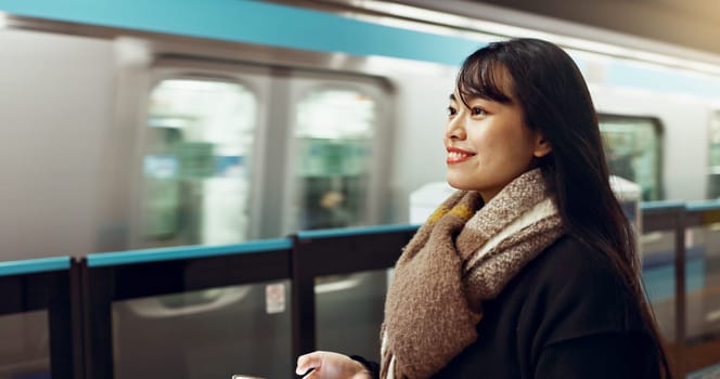 Japanese woman, phone and train station for transport with app, waiting and happy for travel in metro. Girl, smartphone and smile for commute with locomotive for journey, social media or web in Tokyo