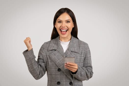 Excited woman with phone celebrating success in houndstooth jacket